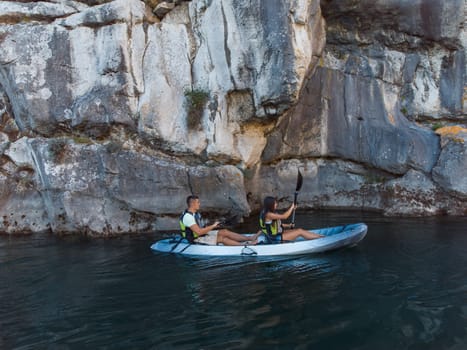 A young couple enjoying an idyllic kayak ride in the middle of a beautiful river surrounded by forest greenery.