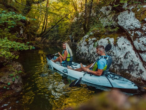 A young couple enjoying an idyllic kayak ride in the middle of a beautiful river surrounded by forest greenery.