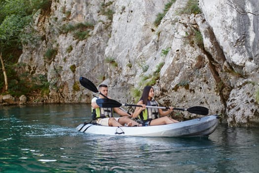 A young couple enjoying an idyllic kayak ride in the middle of a beautiful river surrounded by forest greenery.