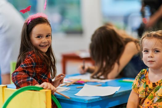 Creative kids during an art class in a daycare center or elementary school classroom drawing with female teacher