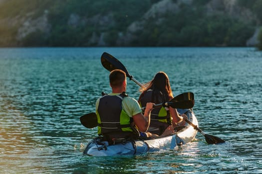 A young couple enjoying an idyllic kayak ride in the middle of a beautiful river surrounded by forest greenery in sunset time.