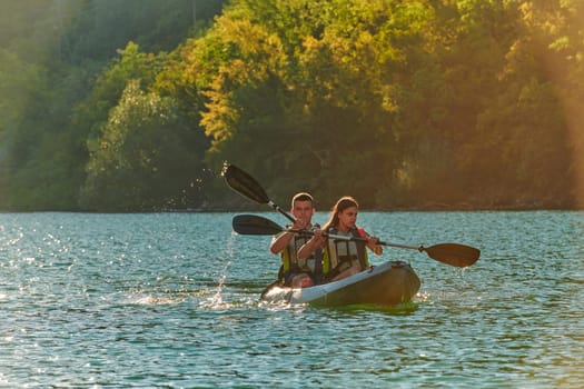 A young couple enjoying an idyllic kayak ride in the middle of a beautiful river surrounded by forest greenery in sunset time.