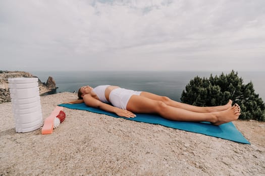 Woman sea pilates. Sporty, middle-aged woman practicing pilates in park near the sea. trains on a yoga mat and exudes a happy and active demeanor, promoting the idea of a healthy lifestyle through exercise and meditation.