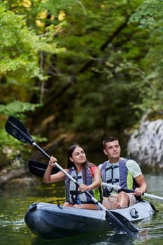 A young couple enjoying an idyllic kayak ride in the middle of a beautiful river surrounded by forest greenery.