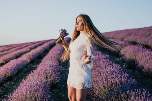 Close up portrait of young beautiful woman in a white dress and a hat is walking in the lavender field and smelling lavender bouquet.