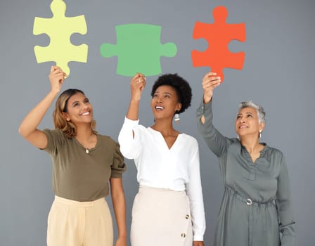 Business people, puzzle pieces and synergy, connection and smile with diversity on studio background. Problem solving, link and working together with teamwork and cooperation with women in corporate.