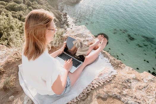 Woman sea laptop. Business woman in yellow hat working on laptop by sea. Close up on hands of pretty lady typing on computer outdoors summer day. Freelance, digital nomad, travel and holidays concept.