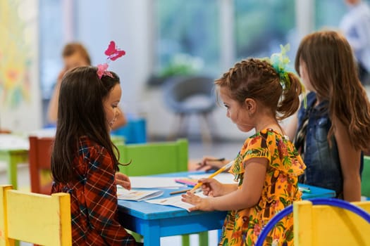 Creative kids during an art class in a daycare center or elementary school classroom drawing with female teacher