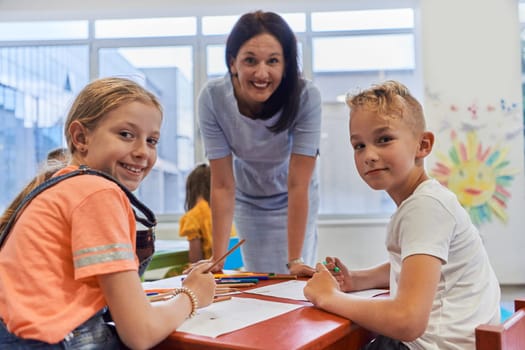 Creative kids during an art class in a daycare center or elementary school classroom drawing with female teacher