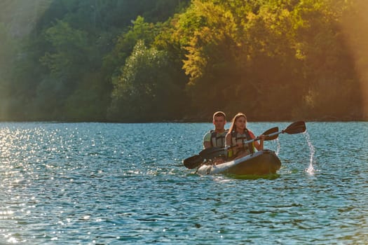 A young couple enjoying an idyllic kayak ride in the middle of a beautiful river surrounded by forest greenery in sunset time.