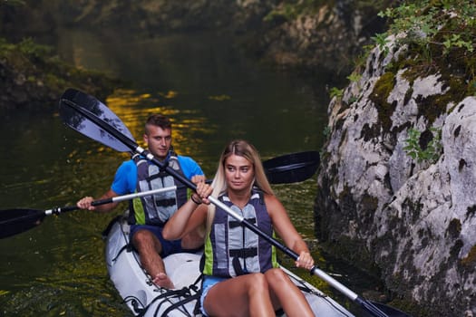 A young couple enjoying an idyllic kayak ride in the middle of a beautiful river surrounded by forest greenery.