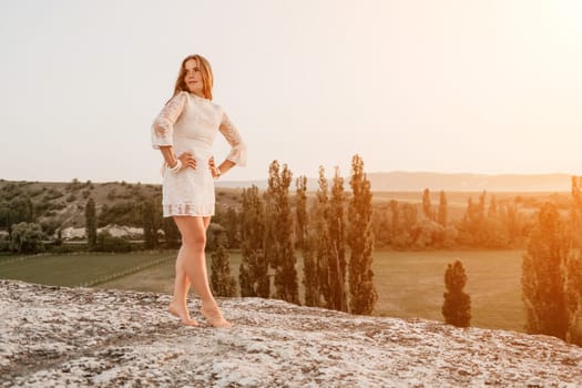 Romantic beautiful bride in white dress posing with sea and mountains in background. Stylish bride standing back on beautiful landscape of sea and mountains on sunset