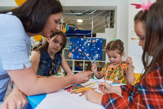 Creative kids during an art class in a daycare center or elementary school classroom drawing with female teacher