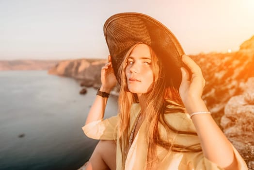 Portrait of happy young woman wearing summer black hat with large brim at beach on sunset. Closeup face of attractive girl with black straw hat. Happy young woman smiling and looking at camera at sea