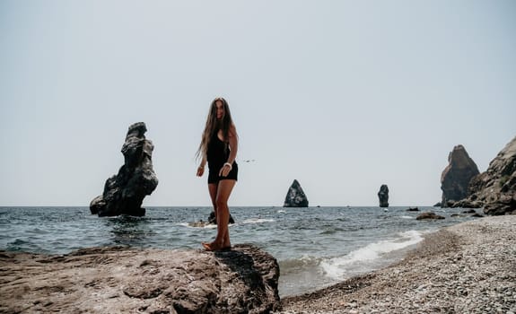 Woman travel sea. Young Happy woman in a long red dress posing on a beach near the sea on background of volcanic rocks, like in Iceland, sharing travel adventure journey