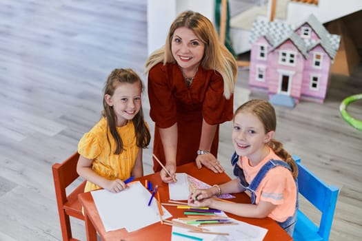 Creative kids during an art class in a daycare center or elementary school classroom drawing with female teacher