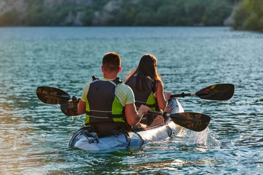 A young couple enjoying an idyllic kayak ride in the middle of a beautiful river surrounded by forest greenery in sunset time.