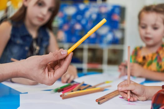 Close up photo of kids during an art class in a daycare center or elementary school classroom drawing with female teacher