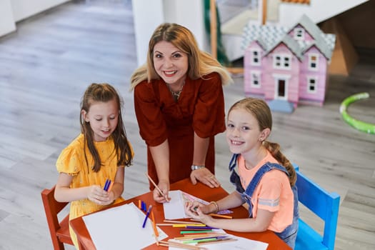 Creative kids during an art class in a daycare center or elementary school classroom drawing with female teacher