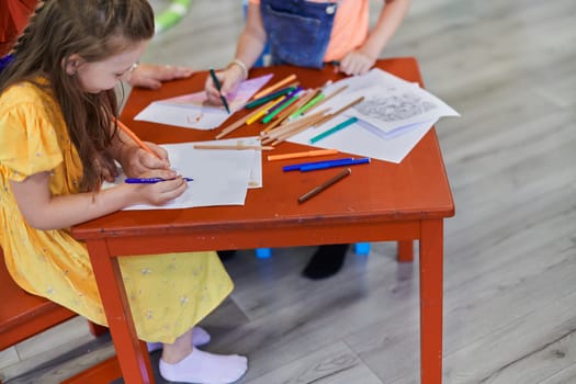 Close up photo of kids during an art class in a daycare center or elementary school classroom drawing with female teacher