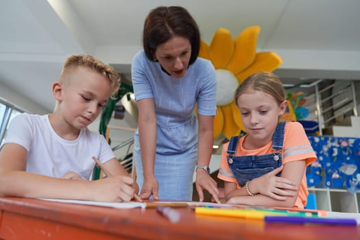 Creative kids during an art class in a daycare center or elementary school classroom drawing with female teacher