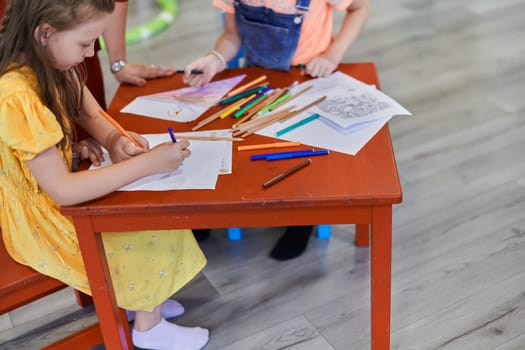 Creative kids during an art class in a daycare center or elementary school classroom drawing with female teacher