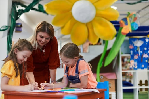 Creative kids during an art class in a daycare center or elementary school classroom drawing with female teacher