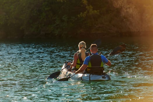 A young couple enjoying an idyllic kayak ride in the middle of a beautiful river surrounded by forest greenery in sunset time.