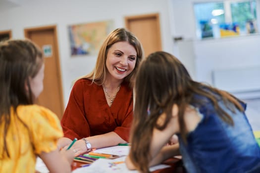 Creative kids during an art class in a daycare center or elementary school classroom drawing with female teacher