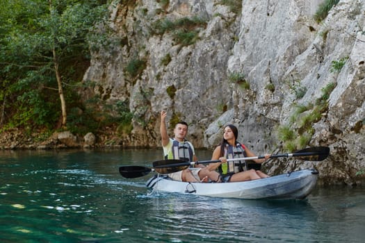 A young couple enjoying an idyllic kayak ride in the middle of a beautiful river surrounded by forest greenery.