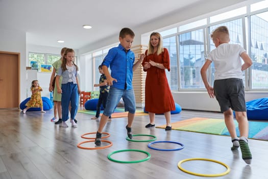 Small nursery school children with female teacher on floor indoors in classroom, doing exercise. Jumping over hula hoop circles track on the floor