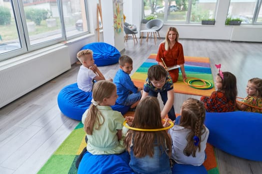 A happy female teacher sitting and playing hand games with a group of little schoolchildren.