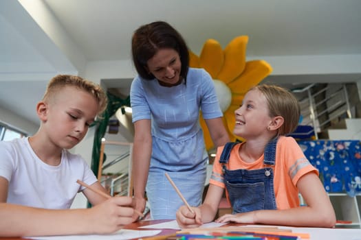 Creative kids during an art class in a daycare center or elementary school classroom drawing with female teacher