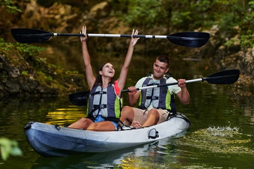 A young couple enjoying an idyllic kayak ride in the middle of a beautiful river surrounded by forest greenery.