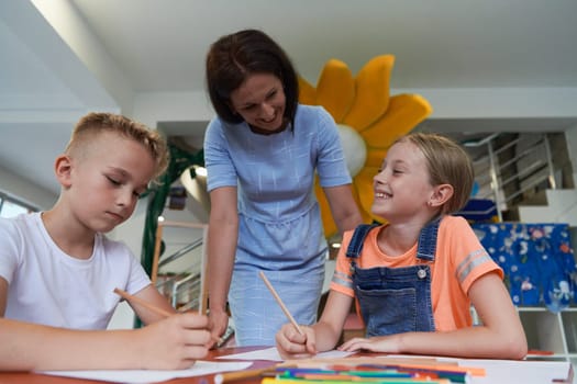 Creative kids during an art class in a daycare center or elementary school classroom drawing with female teacher