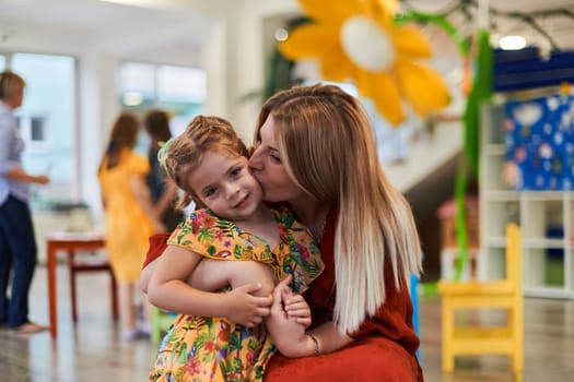 A cute little girl kissing and hugs her mother in preschool. High quality photo