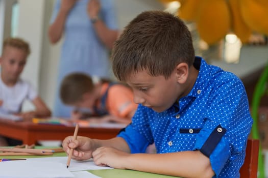 A boy at a preschool institution sits and draws in a notebook with a smile on his face. High quality photo