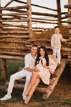 A stylish family in the countryside at sunset. A pregnant woman with her husband and son in nature.