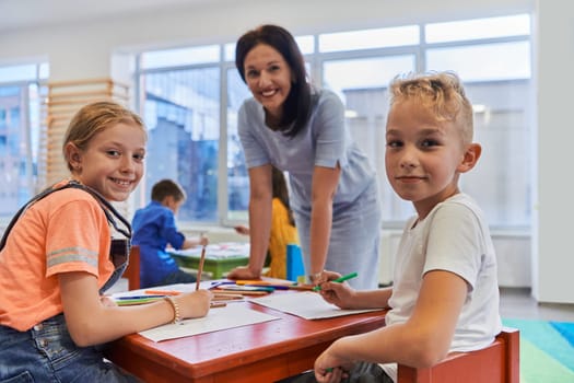 Creative kids during an art class in a daycare center or elementary school classroom drawing with female teacher