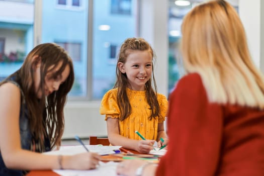 Creative kids during an art class in a daycare center or elementary school classroom drawing with female teacher