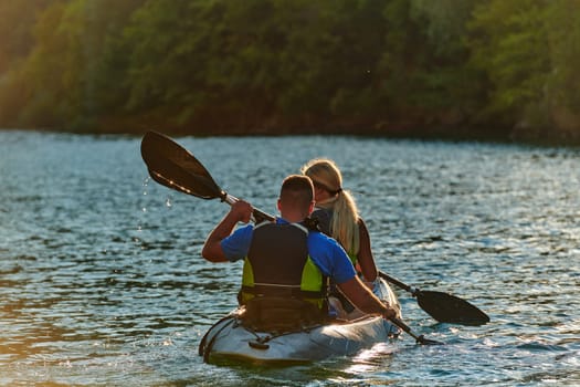 A young couple enjoying an idyllic kayak ride in the middle of a beautiful river surrounded by forest greenery in sunset time.