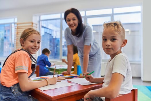 Creative kids during an art class in a daycare center or elementary school classroom drawing with female teacher