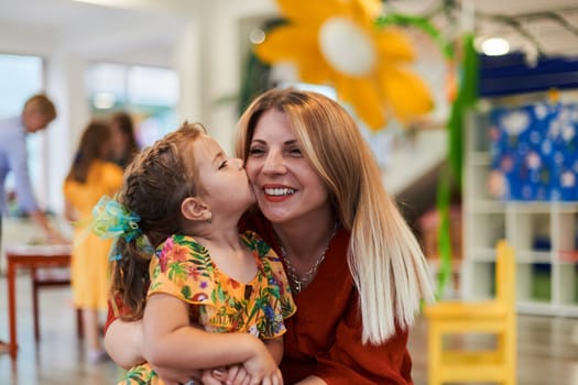 A cute little girl kissing and hugs her mother in preschool. High quality photo