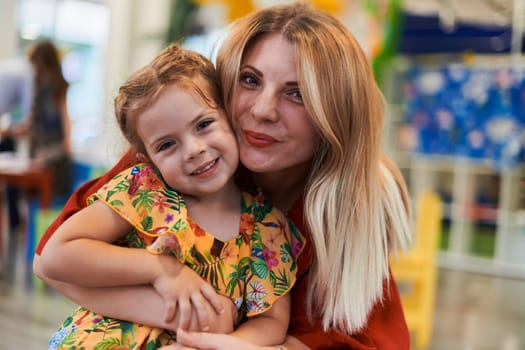 A cute little girl kissing and hugs her mother in preschool. High quality photo