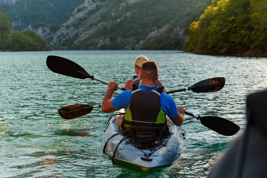 A young couple enjoying an idyllic kayak ride in the middle of a beautiful river surrounded by forest greenery in sunset time.