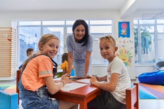 Creative kids during an art class in a daycare center or elementary school classroom drawing with female teacher