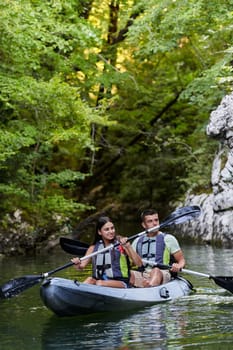 A young couple enjoying an idyllic kayak ride in the middle of a beautiful river surrounded by forest greenery.