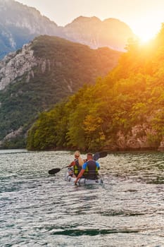 A young couple enjoying an idyllic kayak ride in the middle of a beautiful river surrounded by forest greenery in sunset time.