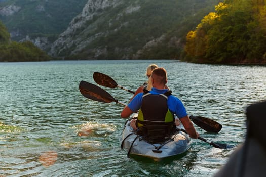 A young couple enjoying an idyllic kayak ride in the middle of a beautiful river surrounded by forest greenery in sunset time.