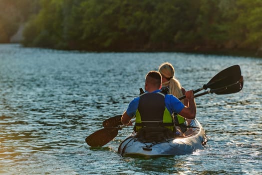 A young couple enjoying an idyllic kayak ride in the middle of a beautiful river surrounded by forest greenery in sunset time.